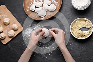 Woman making dumplings (varenyky) with potato at black table, top view