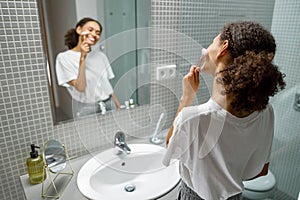 Woman making face massage using face roller with quartz stone in bathroom. Natural cosmetics concept photo