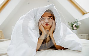 a woman is making a funny face while laying under a blanket on a bed