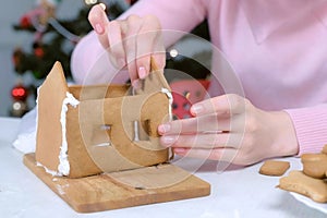 Woman making gingerbread house glues details sugar sweet icing, hands closeup.