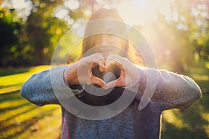 Woman making heart hand sign in the park before sunset