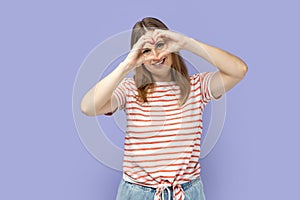 Woman making heart shape with hands in front of her eyes, expressing love, friendship, care.