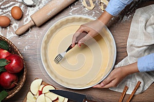 Woman making holes in raw dough with fork at table, top view. Baking apple pie