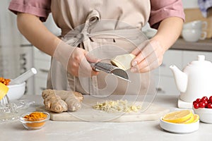 Woman making immunity boosting drink with grated ginger at marble table, closeup