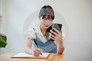 A woman making lists in her notebook while using her smartphone, sitting at a table indoors