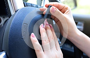 Woman is making manicure in the car. Girl applying  nail polish behind the wheel. Dangerous situation on the road