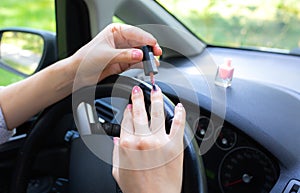 Woman is making manicure in the car. Girl applying  nail polish behind the wheel. Dangerous situation on the road