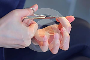 Woman is making manicure at home cutting cuticle using scissors, hands closeup.