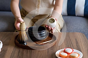 Woman making matcha green tea drink at home using tea ceremony set