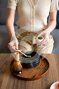 Woman making matcha green tea drink at home using tea ceremony set