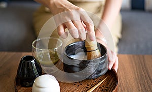 Woman making matcha green tea drink at home using tea ceremony set