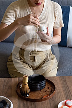 Woman making matcha green tea drink at home using tea ceremony set
