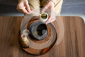 Woman making matcha green tea drink at home using tea ceremony set