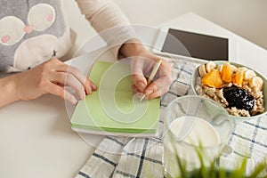 Woman making notes in notepad with healthy food on table