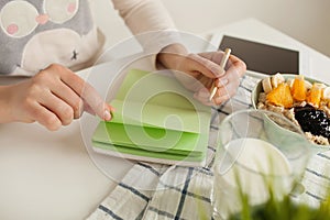 Woman making notes in notepad with healthy food on table