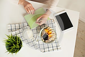 Woman making notes in notepad with healthy food on table