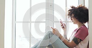 Woman is making online payment bank card using smartphone sitting near window.