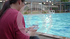 Woman making online payment with credit card and smartphone near the swimming pool.
