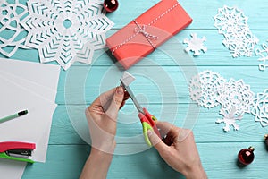 Woman making paper snowflake at turquoise wooden table, top view