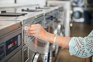 Woman making payment putting quarter to washing laundromat machine in public laundry