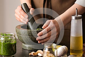 Woman making pesto sauce with mortar and pestle on table in kitchen