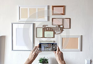 Woman making photo of white wall with set of different empty vertical and horizontal picture frames