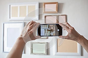 Woman making photo of white wall with set of different empty vertical and horizontal picture frames