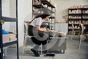 Woman making pot using pottery wheel in creative studio