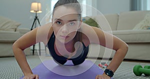 Woman making push-ups exersice on mat from knees at home in living room. Home workout, training and wellness concept.