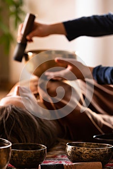 Woman making relaxing massage, meditation, sound therapy with tibetian singing bowls. Stress relief. Selective focus on bowl.