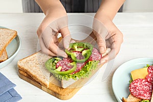 Woman making sandwich with green bell pepper and sausage at white table