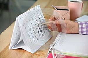 Woman making schedule using calendar at table