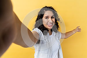 Woman making selfie on her smart phone, showing welcome gesture, broadcasting livestream.