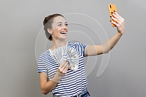 Woman making selfie with money, hiding face behind fan of hundred dollar bills, bragging with income photo