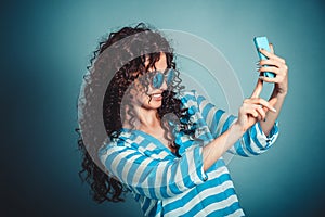 Woman making selfie with smartphone isloated on blue background