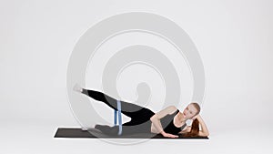 Woman Making Side Leg Lift Exercise With Elastic Rubber Band In Studio