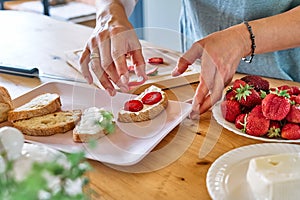 Woman making summer strawberry sandwich. Female hands putting slices of ripe red strawberry on toast with spread stracchino cheese