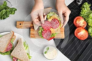Woman making tasty sandwich with sausage at grey marble table, top view