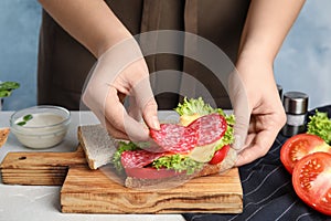 Woman making tasty sandwich with sausage at table