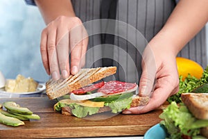 Woman making tasty sandwich with sausage at  table, closeup