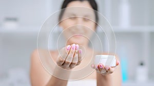 Woman making testing white creamy foundation from jar and showing cream or mask