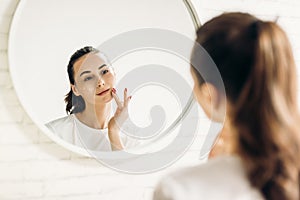 The woman is making up in the bathroom. Woman in bathroom applying cream on face