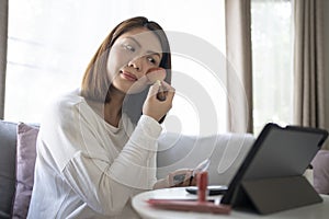 Woman making up her face follow from tablet in living room at home