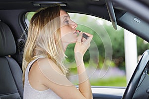 woman making up lips with red lipstick in car