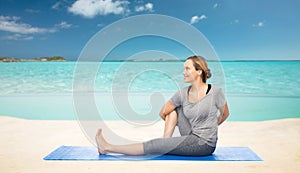 Woman making yoga in twist pose on mat over beach