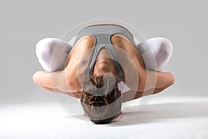 Woman in Malasana with forward bend pose, grey studio background