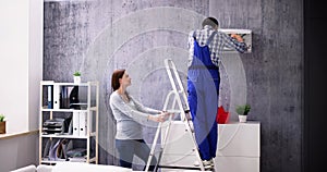 Woman And Male Technician Repairing Air Conditioner