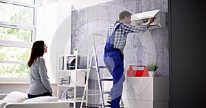 Woman And Male Technician Repairing Air Conditioner