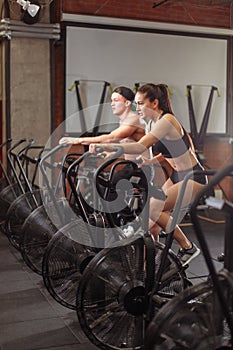 Woman and man biking in gym, exercising legs doing cardio workout cycling bikes