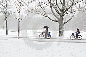 A woman and man biking in a snowy Vondelpark.